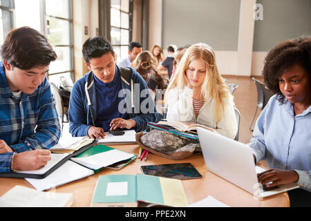 Gli studenti delle scuole superiori utilizzando laptop e tablet digitale lavorando con insegnanti di sesso femminile a scrivania Foto Stock