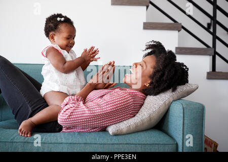 Madre sdraiato sul divano di casa a giocare battendo le mani di gioco con la nostra bambina Foto Stock