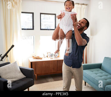 Padre in piedi nel salotto di casa il sollevamento bimba in aria Foto Stock