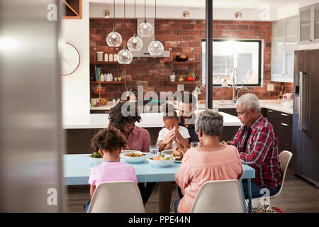 Multi generazione Famiglia Pregare prima del pasto intorno al tavolo a casa Foto Stock