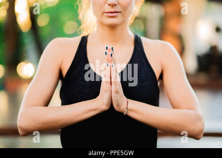 Concentrato ragazza seduta in lotus posano con le mani in namaste e meditando o pregando. Giovane donna con aspetto orientale a praticare yoga da soli su Foto Stock