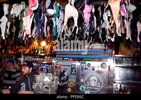 Il barista del bar dello studente pub 'Sehnsucht' in Amalienstraße, Maxvorstadt a Monaco di Baviera. Reggiseni appesa sopra il contatore Foto Stock