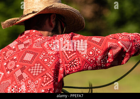 Italiano e cowboy americani, il riscaldamento in un international rodeo show. Vintage nostalgia in una giornata di sole al ranch. Redshirt, jeans blu, gli uomini. Foto Stock