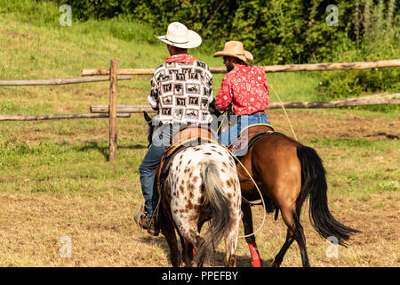 Italiano e cowboy americani, il riscaldamento in un international rodeo show. Vintage nostalgia in una giornata di sole al ranch. Redshirt, jeans blu, gli uomini. Foto Stock