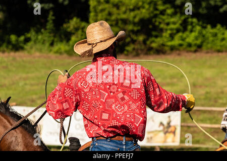 Italiano e cowboy americani, il riscaldamento in un international rodeo show. Vintage nostalgia in una giornata di sole al ranch. Redshirt, jeans blu, gli uomini. Foto Stock