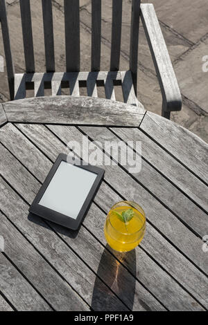 E-reader e un bicchiere di bevanda a base di frutta su un tavolo di legno. Foto Stock