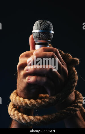 La libertà di parola, immagine concettuale con maschio persona in possesso di un microfono con le mani legate in corde, bassa immagine chiave Foto Stock