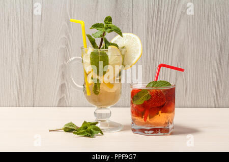 Il freddo estivo rinfrescante limonata mojito con le fette di limone e menta in un bicchiere alto e fragola limonata con la menta in una corta Foto Stock