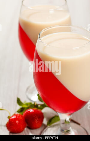 La ciliegia e la gelatina di latte nei bicchieri con foglie di menta e fragole sullo sfondo Foto Stock