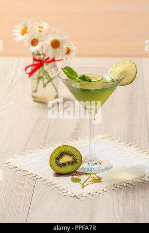 Gelatina di kiwi con pezzi di lime in vetro e bouquet di chamomiles sullo sfondo di legno Foto Stock