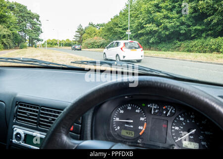 Vista guardando attraverso un parabrezza di automobile mentre si è in attesa di svoltare a sinistra in corrispondenza di una giunzione, visto dalla posizione del conducente all'interno del veicolo, England, Regno Unito Foto Stock