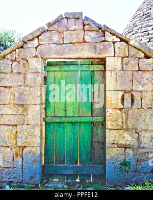 Antichi verde porta di legno su un vecchio muro di pietra accanto a un trullo Foto Stock