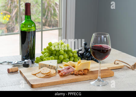 Bicchiere di vino rosso con bottiglia di vino, formaggio, cracker, prosciutto, mandorle e uva Foto Stock