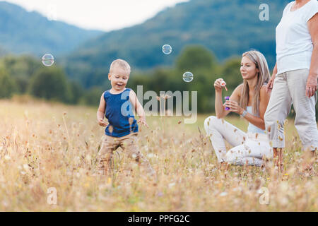 Bambino felice con la famiglia avente un grande tempo a soffiare bolle all'aperto Foto Stock