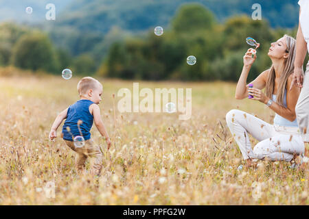 Bambino felice con la famiglia avente un grande tempo a soffiare bolle all'aperto Foto Stock