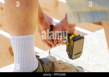 Uomo bello carpenter l'installazione di un pavimento in legno terrazza esterna in casa di nuova costruzione patio. Foto Stock