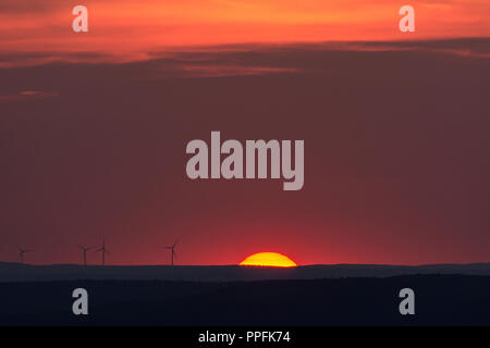 Sole incandescente e sagome di turbine eoliche all'orizzonte, il tramonto, Baviera, Germania Foto Stock