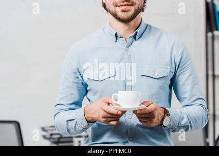 Ritagliato shot del giovane imprenditore con tazza di caffè presso un ufficio moderno Foto Stock