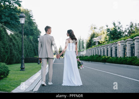 Vista posteriore della sposa e lo sposo per mano e camminare sulla strada Foto Stock