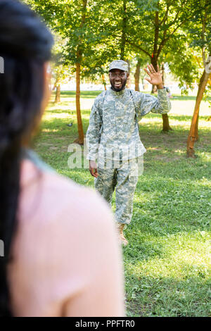 Immagine ritagliata di sorridere african soldato americano in uniforme militare agitando la mano per ragazza in posizione di parcheggio Foto Stock