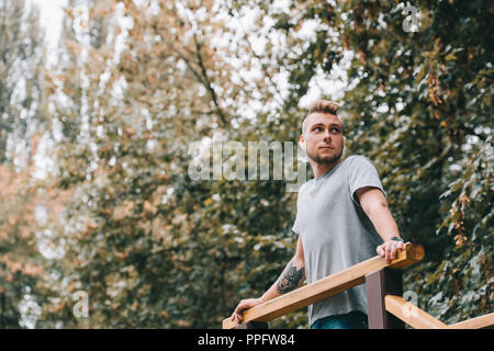 Giovane uomo tatuato appoggiata sulle ringhiere in autunno park Foto Stock