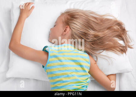 Rilassati piccolo bambino giace su stomaco, giace sul morbido cuscino, essendo nel profondo sonno, giace sul cuscino bianco, luce ha i capelli dritti, gode la comodità e la pace Foto Stock