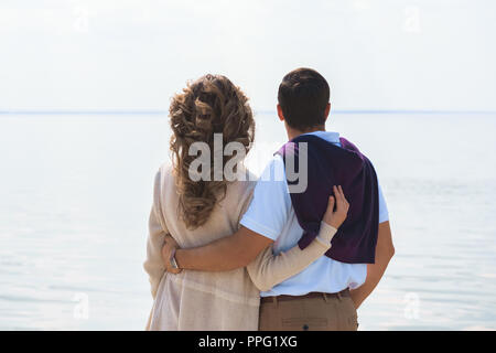 Vista posteriore della coppia romantica abbracciando e guardando il mare Foto Stock