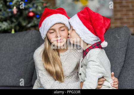 Carino piccolo ragazzo in santa hat baciare la sorella del tempo di Natale Foto Stock