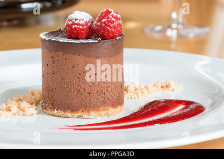 Mousse al cioccolato sulla piastra bianca decorata con 2 lamponi sulla parte superiore e coperti da zucchero in polvere. La lastra decorata da biscotto e raspber Foto Stock