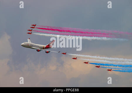 Virgin Atlantic Boeing 747 Jumbo Jet aereo volare in formazione con RAF Royal Air Force frecce rosse display team getti di fumo di tallonamento. Airshow. Compagnia aerea Foto Stock