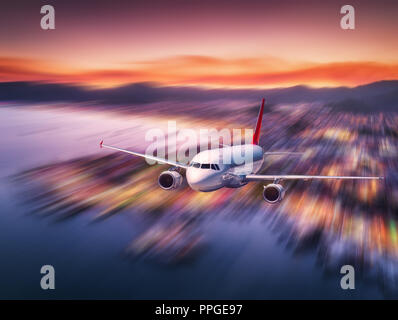 In aereo con motion blur effetto è volare sulla costa del mare di notte. Paesaggio con aereo passeggeri, offuscata edifici, illuminazione della città, del mare e s Foto Stock