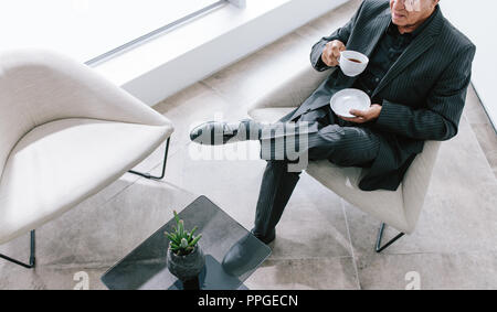 Vista superiore del businessman senior seduto in salotto ufficio avente il caffè. Imprenditore maschio avente pausa caffè in ufficio. Foto Stock