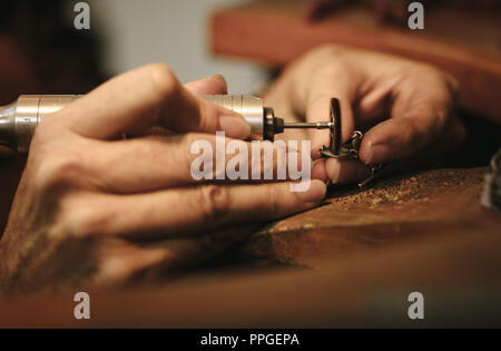 Le mani del gioielliere femmina la lucidatura di un gioiello con macchina rettificatrice. Goldsmith facendo un pezzo di gioielli al suo banco. Foto Stock