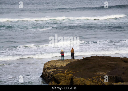 Due anziani pescatori di surf cast per la sabbia pesce persico off il barnacle coperto rocce lungo il litorale dell'Oceano Pacifico in Yachats, Oregon Foto Stock