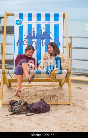 Aberystwyth Wales UK, mercoledì 26 settembre 2018 UK Meteo: due giovani donne seduto in una sedia sdraio gigante su Aberystwyth prmenade godendo di un pomeriggio di sole caldo sulla West Wales coast © Keith Morris / Alamy Live News Foto Stock