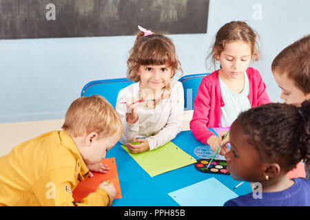 Bambini vernice con acquarello e pennello in asilo nido nel disegno classe o classe di pittura Foto Stock