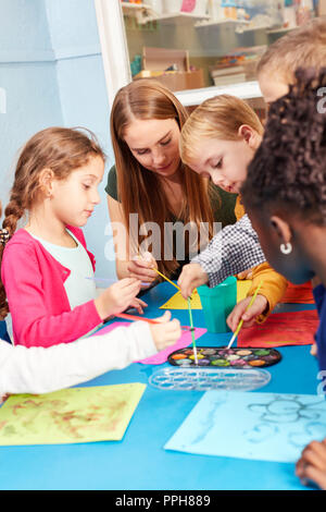 Pittura per bambini nella classe di pittura con acquarello e spazzola sotto la supervisione di un insegnante di scuola materna Foto Stock