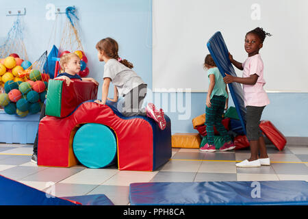 Un gruppo di bambini nella palestra dell'asilo o di età prescolare durante la riproduzione e la ginnastica Foto Stock