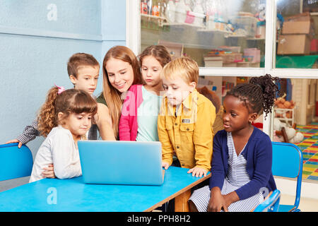 Kindergartner o un insegnante con bambini al computer portatile in una scuola materna Foto Stock