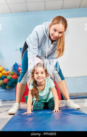 Donna sport come un insegnante aiuta ragazza mentre facendo ginnastica in palestra nella scuola elementare Foto Stock