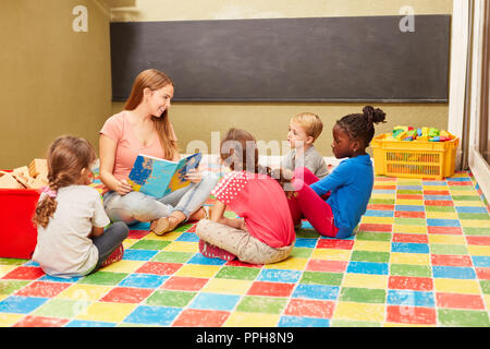 Un gruppo di bambini e insegnanti la lettura di un libro da favola in day care center Foto Stock