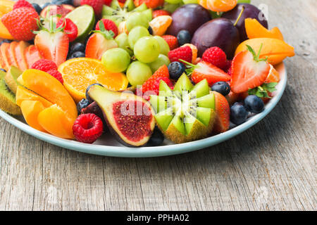 Una sana frutta e bacche platter, Fragole Lamponi arance Prugne Mele Kiwi uve mirtilli sul grigio scuro tavolo in legno, close up, cop Foto Stock
