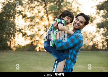 Uomo sorridente giocando con il suo felice figlio mediante il sollevamento di lui nel parco. Foto Stock