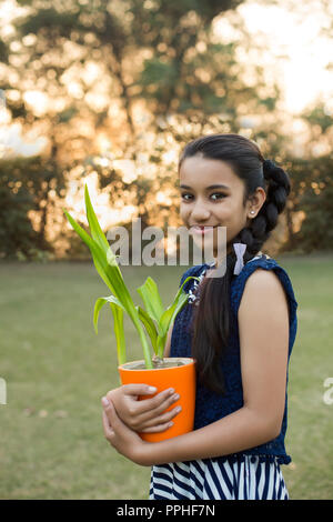 Sorridente ragazza tenendo un piccolo vaso di fiori in mano in piedi nel parco. Foto Stock