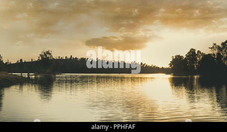 Tramonto sul lago con la luce del sole illuminando le nuvole e riflessi nell'acqua Foto Stock