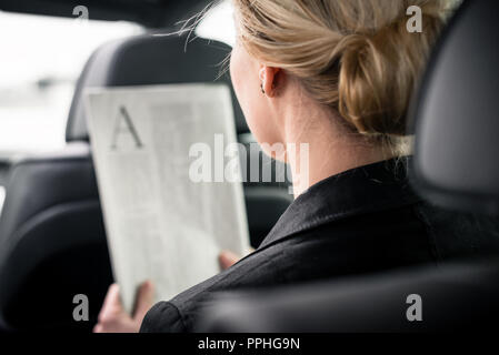 Vista posteriore di imprenditrice leggendo il giornale in auto Foto Stock