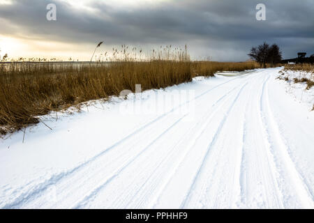 La neve sulla strada, paesaggio invernale con moody sky prima del tramonto sul lago Foto Stock