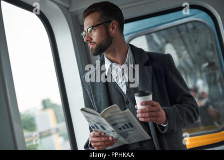 Viaggio di affari. Giovane imprenditore in piedi in treno quotidiano di contenimento e la coppa di bere il caffè caldo godendo la vista della finestra close-up Foto Stock