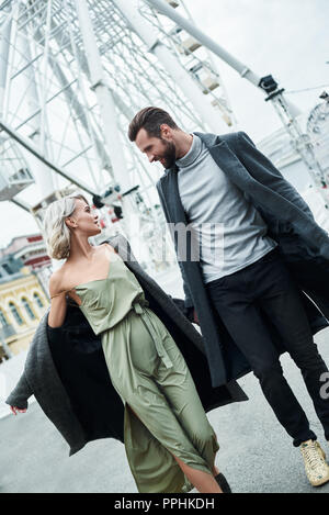 Data romantico all'esterno. Coppia giovane passeggiate al parco divertimento tenendo le mani parlando di sorridere gioiosa Foto Stock