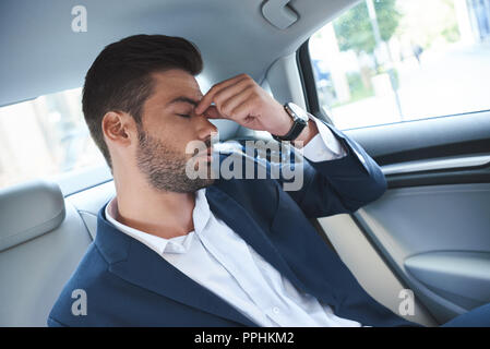 Un giovane uomo è sconvolto e si siede nella cabina di grigio di un auto di lusso Foto Stock